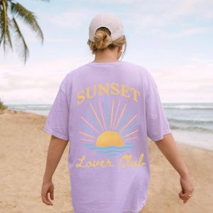 May include: A lavender t-shirt with a graphic of a sunset and the text "Sunset Lover Club".