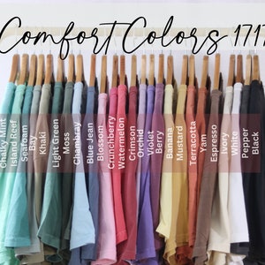 May include: A rack of 17 different colored t-shirts, labeled with the names of the colors, including Chalky Mint, Island Reef, Seafoam, Bay, Khaki, Light Green, Moss, Chambray, Blue Jean, Blossom, Crunchberry, Watermelon, Crimson, Orchid, Violet, Berry, Banana, Mustard, Terracotta, Yam, Espresso, Ivory, White, Pepper, and Black. The rack is labeled "Comfort Colors 1717".