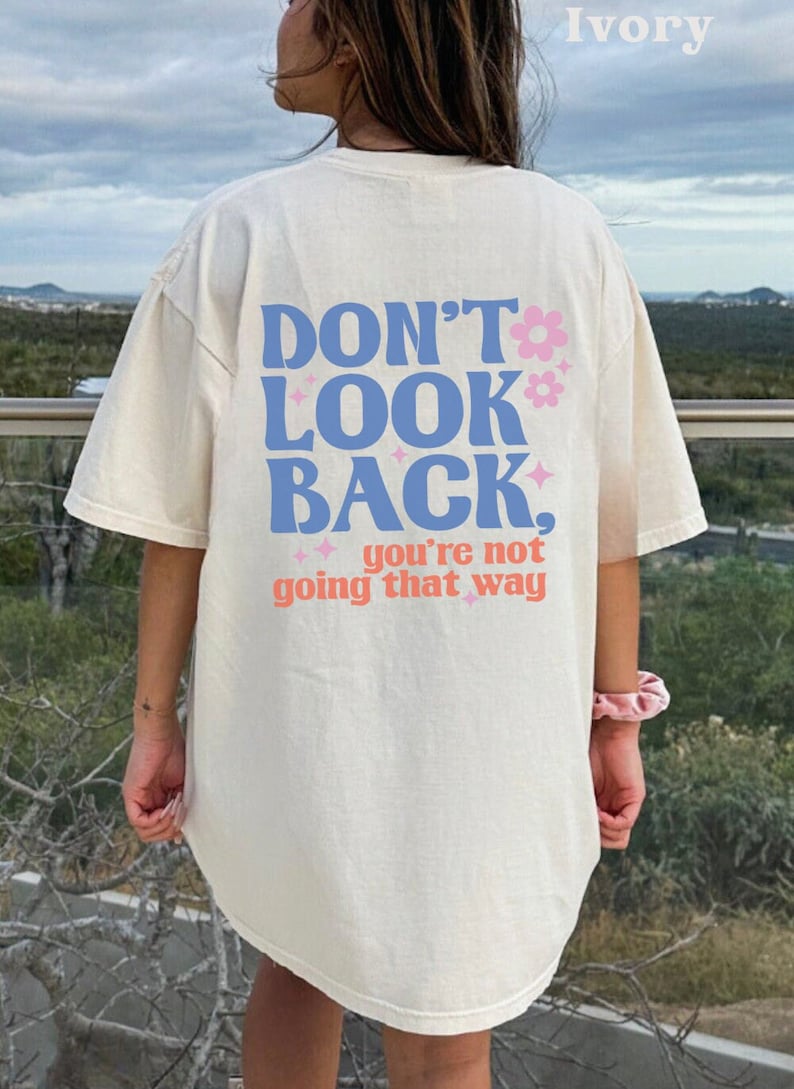 May include: Ivory colored t-shirt with a blue and pink graphic that says "Don't Look Back, you're not going that way".