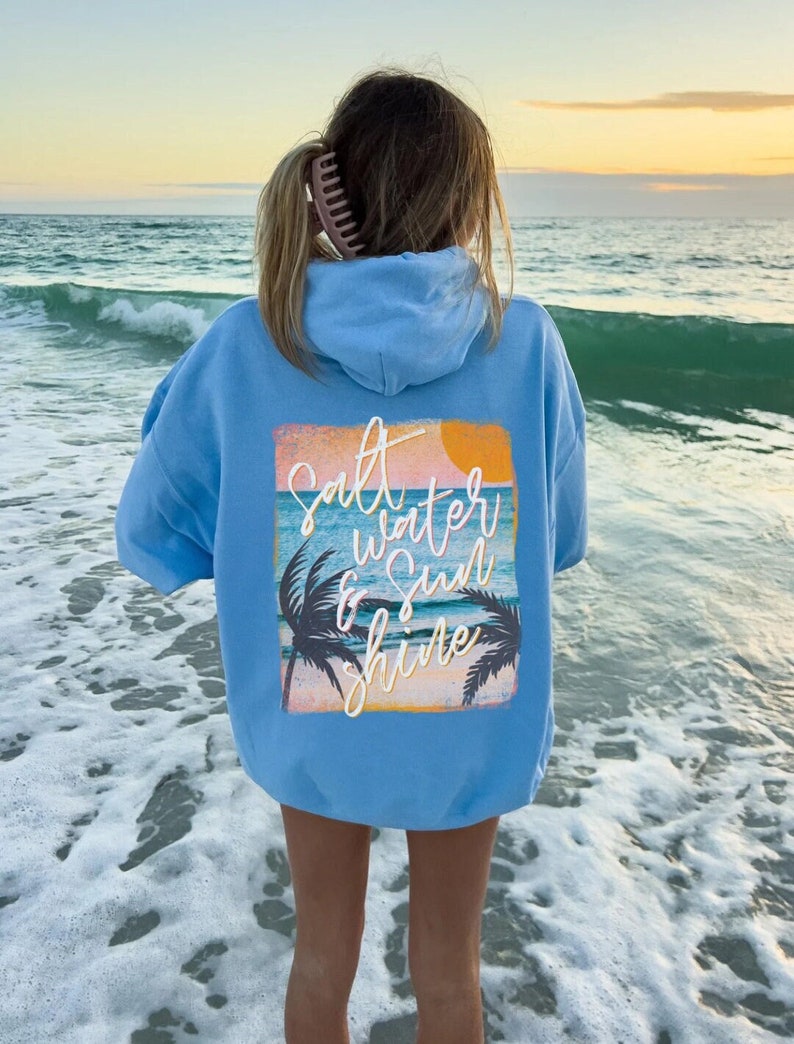 May include: A light blue hoodie with a graphic print on the back that says "Salt Water & Sun Shine" with a sunset and palm trees.