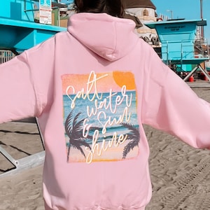 May include: Pink hoodie with a graphic print of a sunset, palm trees, and the text "Salt Water & Sun Shine".
