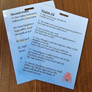 May include: Two blue laminated cards with rounded corners and holes punched in the top right corner. The cards contain the text of Psalm 23 and The Lord's Prayer. The cards have a red and white graphic of a cross and lungs on the bottom right corner.