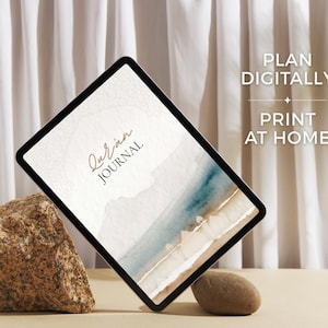May include: A digital tablet displaying a Quran Journal cover with a watercolor landscape of blue water and sandy shores. The screen features the text Quran Journal. To the right, the text reads PLAN DIGITALLY PRINT AT HOME with a small star icon.