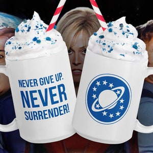 May include: Two white ceramic mugs with blue and white designs. One mug has a blue and white planet design with the text "NEVER GIVE UP. NEVER SURRENDER!" on the other mug.