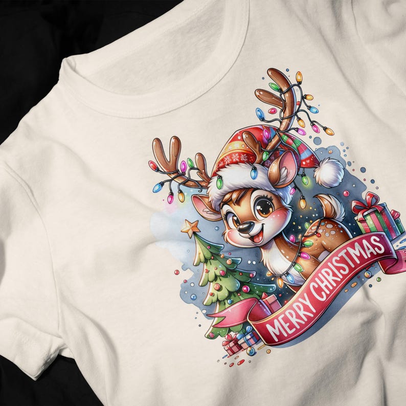 May include: A white t-shirt with a cartoon reindeer wearing a Santa hat and surrounded by Christmas lights, a small Christmas tree, and presents. The text "Merry Christmas" is written on a red ribbon.