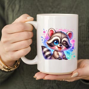 Pu&ograve; includere: Tazza in ceramica bianca con un disegno di procione dei cartoni animati. Il procione ha gli occhi blu e fa l'occhiolino, con la lingua di fuori. Lo sfondo presenta schizzi colorati. La tazza &egrave; tenuta da una persona.