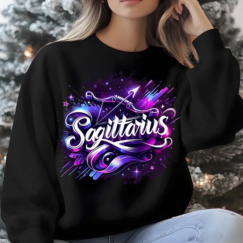 Peut inclure: Sweat-shirt noir avec un motif graphique color&eacute; du signe du zodiaque Sagittaire. Le motif repr&eacute;sente un arc et une fl&egrave;che dans un sch&eacute;ma de couleurs violet, bleu et blanc. Le mot "Sagittaire" est &eacute;crit dans une police de caract&egrave;res stylis&eacute;e.