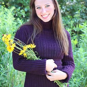 May include: A dark purple turtleneck sweater with a textured knit pattern. The sweater is paired with matching pants. The person is holding a bouquet of yellow flowers.