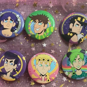 Puede incluir: Seis botones redondos y coloridos con ilustraciones de personajes de estilo anime. Los botones tienen varios colores de fondo, incluyendo morado, verde, rosa y azul, con retratos detallados de personajes. Los botones son probablemente para fans de la serie de anime.