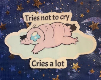 Op de afbeelding: Een sticker met een lichtroze cartoonfiguur met een traanvormig oog, liggend op een wolk. De tekst "Tries not to cry" staat boven het personage en "Cries a lot" eronder.