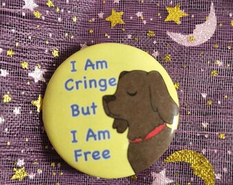 May include: A round yellow pin-back button featuring a brown dog illustration and the blue text "I Am Cringe But I Am Free". The dog is shown in profile facing left, wearing a thin red collar. The design is printed on a smooth, circular surface.
