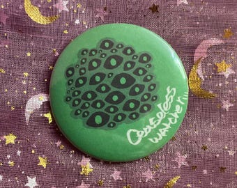 May include: A round, green button featuring a cluster of black and gray eye illustrations. The button has the text "Ceaseless Watcher" in white script. The button is set against a purple background with gold stars and crescent moons.
