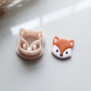 May include: A white plastic fox cookie cutter with a matching orange fondant fox cutout.