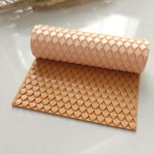 May include: A close-up of a brown silicone rolling pin with a scale pattern. The rolling pin is rolled up and the pattern is visible on the surface.