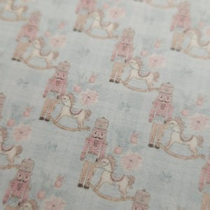 May include: A light blue fabric with a repeating pattern of pink nutcracker soldiers riding rocking horses. The background is a light blue with a subtle floral pattern.