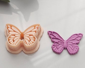 May include: Two butterfly-shaped cookie cutters, one in a light peach color and the other in a light purple color.