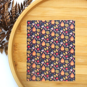 May include: A sheet of decorative paper with a repeating pattern of campfires, apples, pears, leaves, and mugs of hot beverages on a dark blue background.