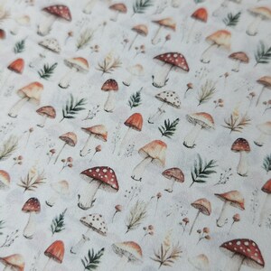 May include: A white background is covered with a pattern of watercolor mushrooms in various sizes and colors. The mushrooms have red, brown, and tan caps with white spots. Green leaves and sprigs of grass are also scattered throughout the design.