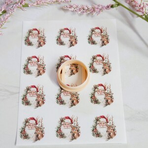May include: A sheet of Christmas-themed stickers featuring Santa Claus with a reindeer, surrounded by a wreath. A beige circular cookie cutter is placed on top of the stickers. The stickers have a vintage, watercolor style.
