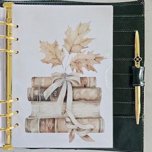 Pode incluir: Uma pilha de livros antigos com um laço branco e uma ilustração em aquarela de folhas de outono sobre um fundo branco.