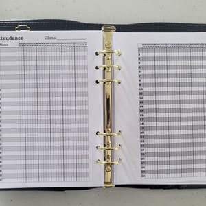 May include: A black leather binder with gold rings and a white page open to a gridded attendance sheet. The sheet has the word "Attendance" and "Class:" printed at the top.