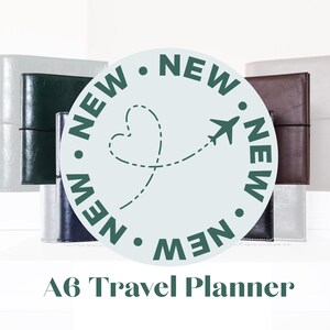 May include: A6 travel planners in various colors, including silver, dark green, navy, and brown. A circular graphic with the word "NEW" repeated around the edge, and a heart-shaped dotted line with an airplane graphic in the center.