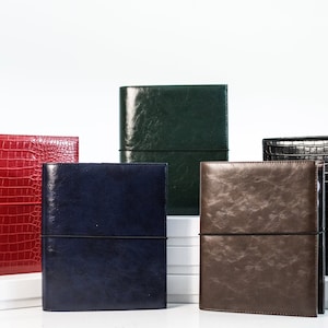 May include: Five leather-bound journals in different colors, including red, green, blue, brown, and black. The journals have elastic bands to keep them closed.