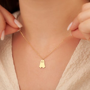 May include: A gold chain necklace with a ghost-shaped pendant. The pendant is a simple silhouette of a ghost with two small circles for eyes.