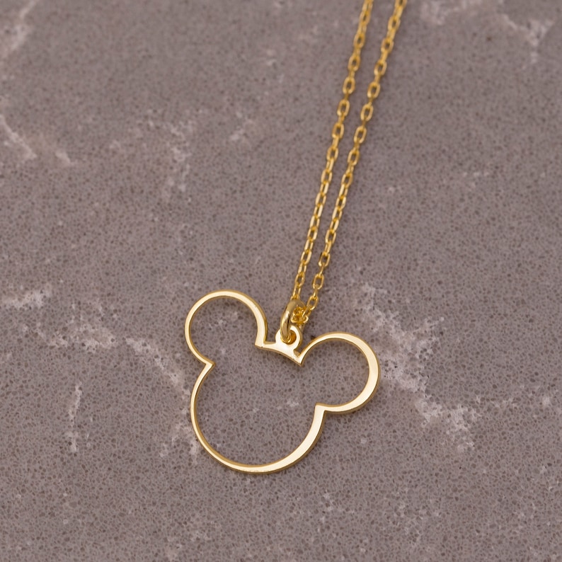May include: A gold chain necklace with a Mickey Mouse head pendant. The pendant is a simple outline of Mickey's head with large ears.
