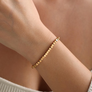 May include: A gold bracelet made of small, square-shaped beads.