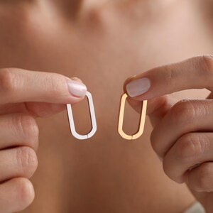 May include: Two oval-shaped earrings, one gold and one silver, held between two fingers.