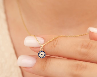 May include: A gold chain necklace with a small, round pendant featuring a blue evil eye design surrounded by white stones.