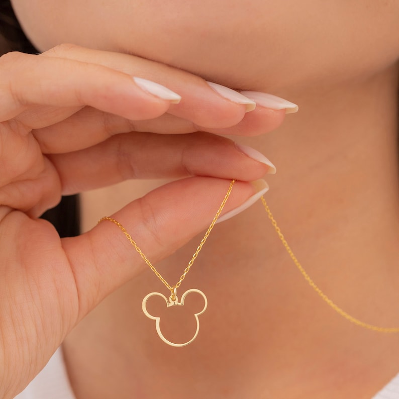 May include: A gold chain necklace with a Mickey Mouse head pendant. The pendant is a simple outline of Mickey's head with large ears.