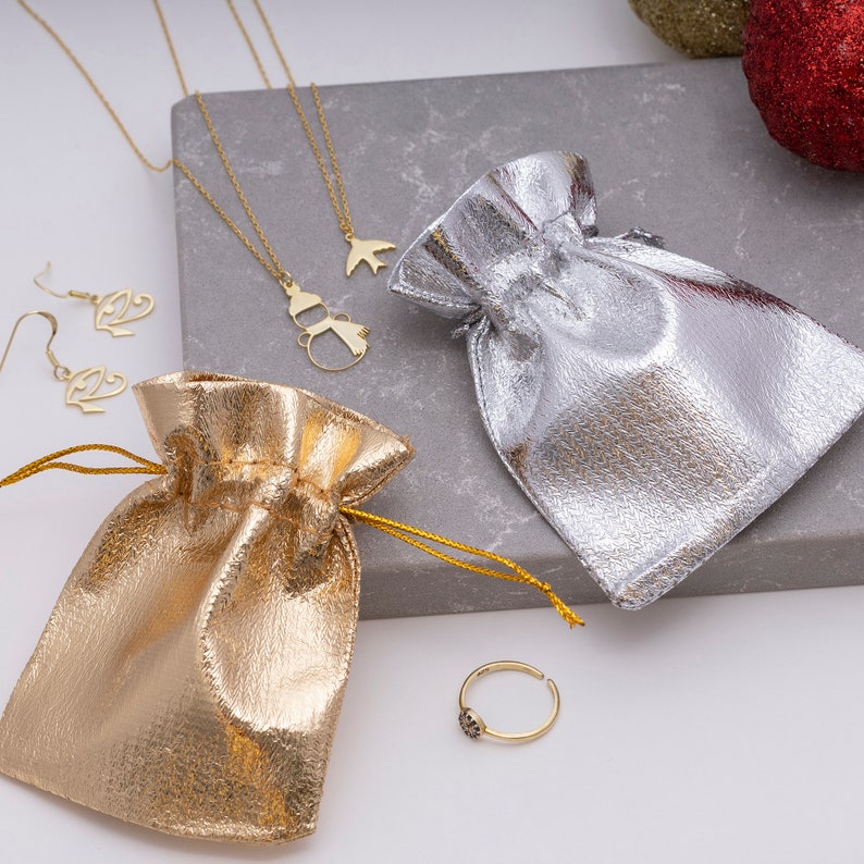 K&ouml;nnte beinhalten: Zwei goldene Schmuckbeutel, einer silber, einer gold, mit einer goldenen Halskette mit einem Schneemann- und Vogelanh&auml;nger, einem Paar goldenen Ohrringen und einem goldenen Ring mit einem schwarzen Stein.