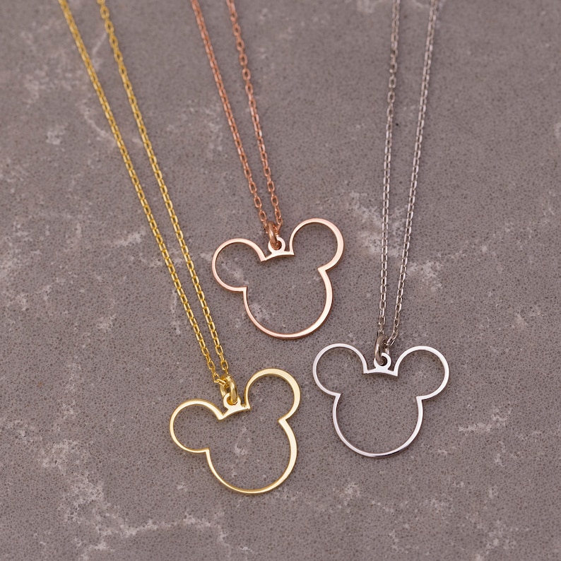 May include: Three gold, silver, and rose gold necklaces with a Mickey Mouse head pendant. The pendants are hollow and have a simple outline.