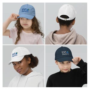 May include: Four baseball caps in light blue, white, and navy, each with the text "BAD DAY TO BE A Blueberry" and a blueberry graphic. The caps are shown on children. The caps have adjustable straps.