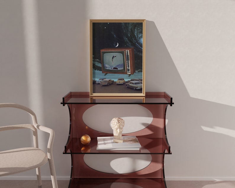 Puede incluir: Una impresi&oacute;n enmarcada de un televisor vintage con un dise&ntilde;o retro, que muestra una escena de coches conduciendo por una carretera con una luna creciente en el cielo. La impresi&oacute;n se muestra en una estanter&iacute;a de vidrio de tres niveles con un dise&ntilde;o redondo y ovalado.