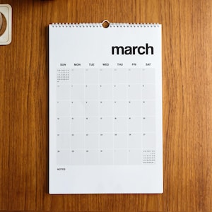 May include: A white wall calendar with black text showing the month of March. The calendar features a grid layout with days of the week labeled from Sunday to Saturday, a spiral binding at the top, and a dedicated section for notes at the bottom.