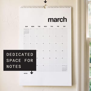 May include: A white wall calendar for the month of March featuring black text, a grid layout for days of the week, a wire hook for hanging, and a dedicated space for notes at the bottom. The calendar displays the month name in bold letters.