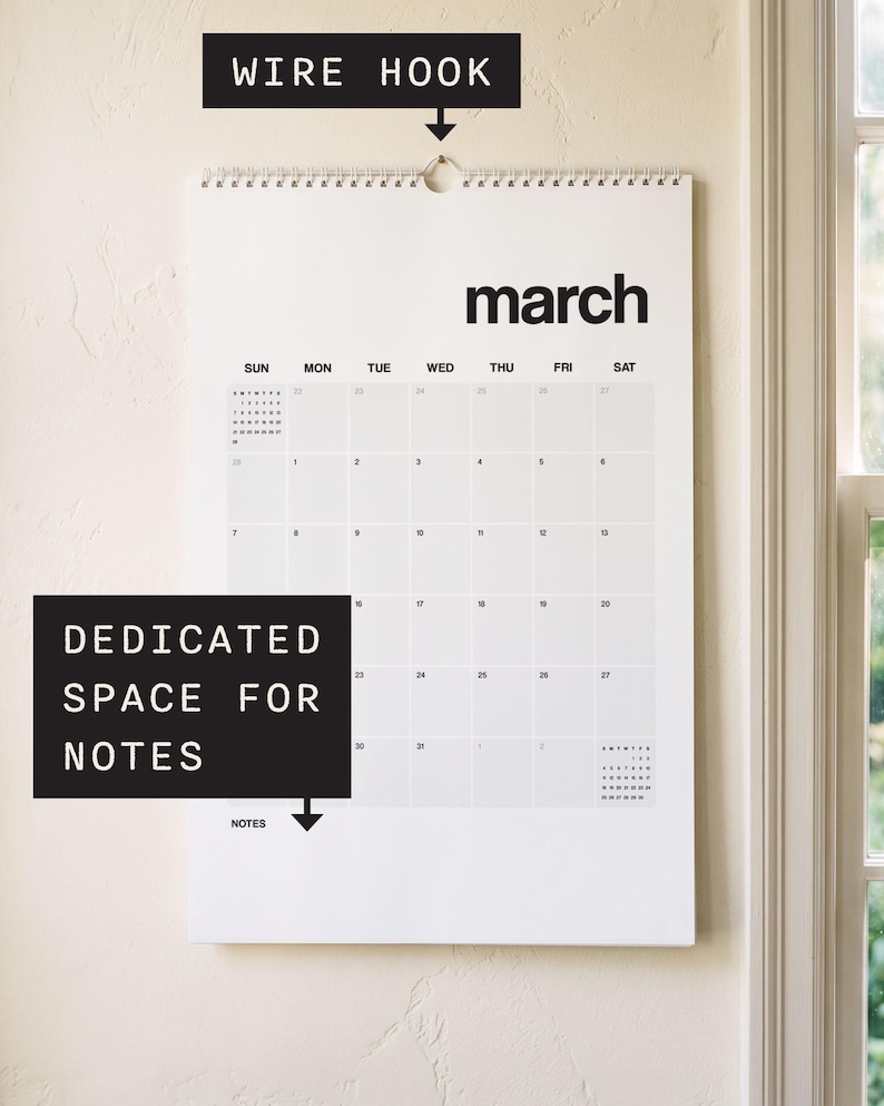 May include: A white wall calendar for the month of March featuring black text, a grid layout for days of the week, a wire hook for hanging, and a dedicated space for notes at the bottom. The calendar displays the month name in bold letters.