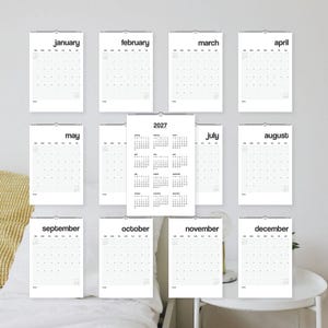 May include: A 2027 wall calendar set featuring twelve individual monthly pages with black sans-serif text on white paper, plus a central overview page displaying all twelve months of the year in a grid format, all bound with wire-o spiral.