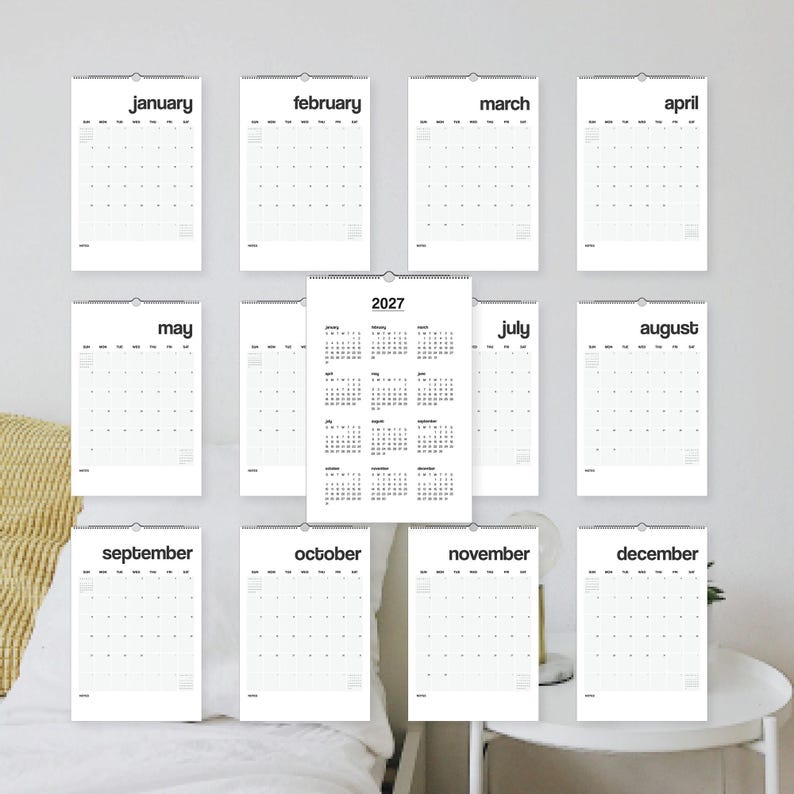 May include: A 2027 wall calendar set featuring twelve individual monthly pages with black sans-serif text on white paper, plus a central overview page displaying all twelve months of the year in a grid format, all bound with wire-o spiral.