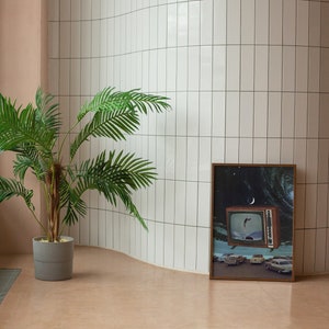 Puede incluir: Una impresi&oacute;n enmarcada de un televisor retro con un pez saltando fuera de la pantalla. El televisor est&aacute; sobre un fondo azul y blanco con estrellas y una luna creciente. La impresi&oacute;n est&aacute; enmarcada en un marco de madera oscura y est&aacute; colgada en una pared de azulejos blancos.