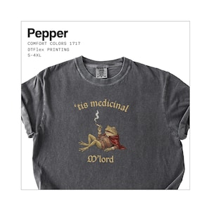 Może przedstawiać: Ciemnoszara koszulka z grafiką żaby palącej papierosa, w pelerynie i napisem "'tis medicinal M'lord". Koszulka ma r&oacute;wnież napis "Pepper", "COMFORT COLORS 1717", "DTFlex PRINTING" i "S-4XL".