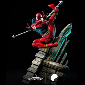 Puede incluir: Una figura de acci&oacute;n roja y azul de un superh&eacute;roe con un dise&ntilde;o de telara&ntilde;a en el pecho, sosteniendo un arma. La figura est&aacute; en una pose de acci&oacute;n din&aacute;mica, de pie sobre una base de piedra. La figura es parte de una serie coleccionable.