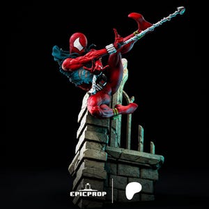 Puede incluir: Una figura de acci&oacute;n roja y blanca de un superh&eacute;roe en una pose din&aacute;mica, sosteniendo un arma en forma de telara&ntilde;a. La figura est&aacute; posada sobre una estructura de piedra con una valla de metal. La figura forma parte de una serie coleccionable.