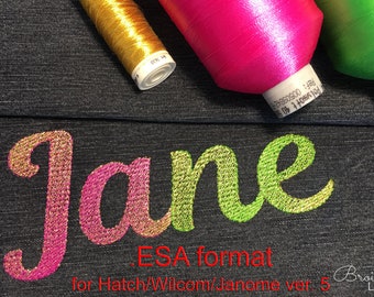 May include: Close-up of the word "Jane" embroidered in gold, pink, and green thread on a dark denim fabric. The word is in a cursive font. Three spools of thread are visible in the background: gold, pink, and green.
