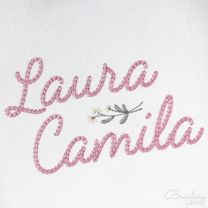May include: Embroidered names "Laura Camila" in pink thread with a small floral design in the center.