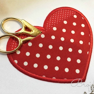 May include: A red heart-shaped fabric pocket with white polka dots, featuring a gold pair of scissors inside.