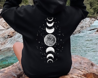 Peut inclure: Sweat-shirt à capuche noir avec un motif de phases de lune blanc au dos. Le motif représente une pleine lune, des croissants de lune et des étoiles.